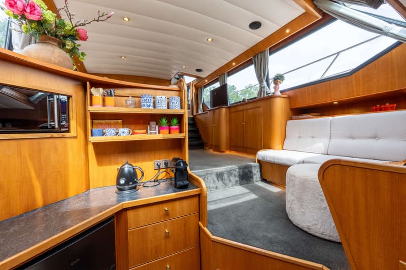 De foto toont het interieur van een boot met een houten afwerking, een zithoek, een kombuis en een trap.