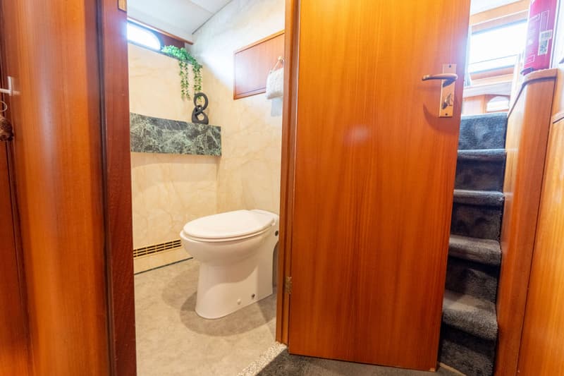 Een interieurfoto toont een toiletruimte met een wit toilet en marmeren wanden, naast een trap met grijze bekleding.