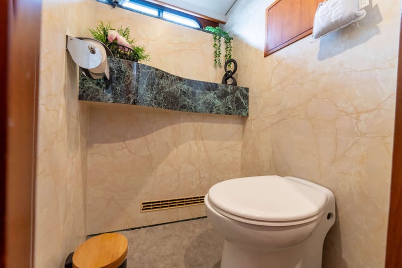 Een toiletruimte met marmeren wanden, een wit toilet, een donkergroene marmeren plank en een raam bovenaan.