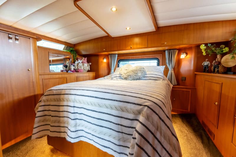 Een slaapkamer met een tweepersoonsbed met gestreepte dekens, houten wanden en kasten, en een raam met gordijnen.