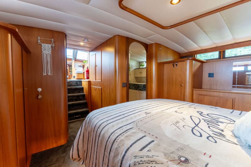 Een slaapkamer in een boot met een bed, houten wanden, een trap en een doorgang naar een badkamer.