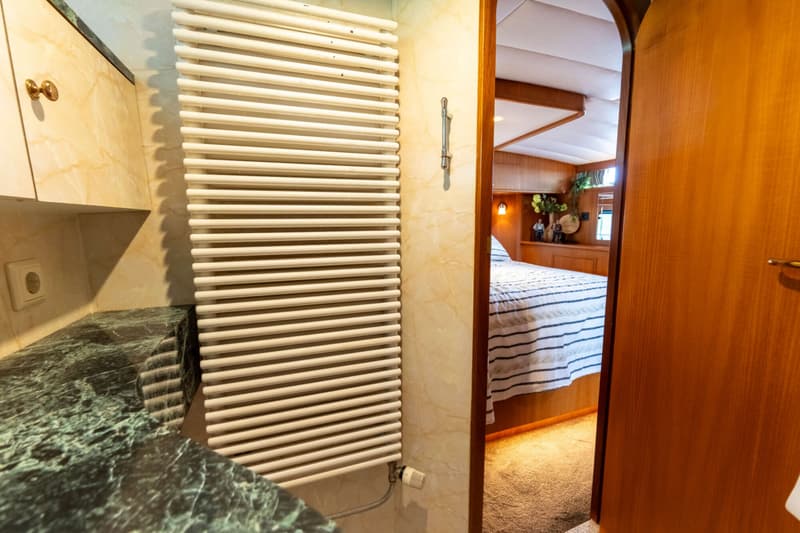 Een witte handdoekradiator hangt aan een marmeren muur naast een open houten deur die leidt naar een slaapkamer.
