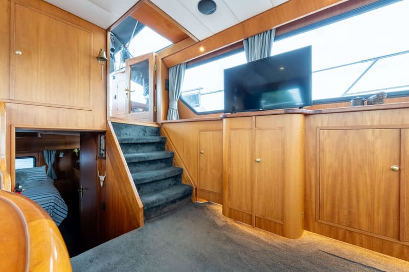 Een interieur van een boot met houten wanden, een trap met donkergrijze bekleding en een televisie op een kast.