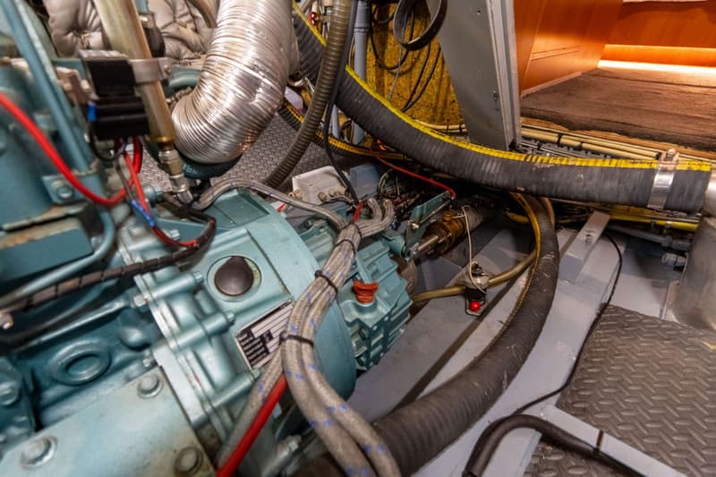 De foto toont een detail van een motorruimte met een turquoise motor, diverse slangen, kabels en leidingen.