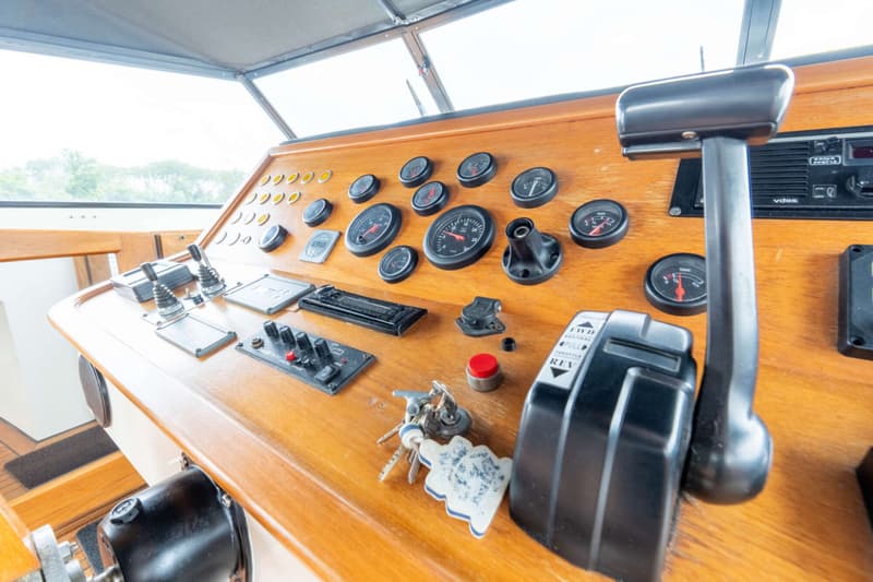 Een houten dashboard met diverse meters, schakelaars, hendels en een sleutelbos is zichtbaar.