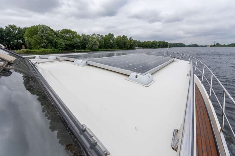 Twee zonnepanelen zijn gemonteerd op het dek van een boot, met bomen en water op de achtergrond.