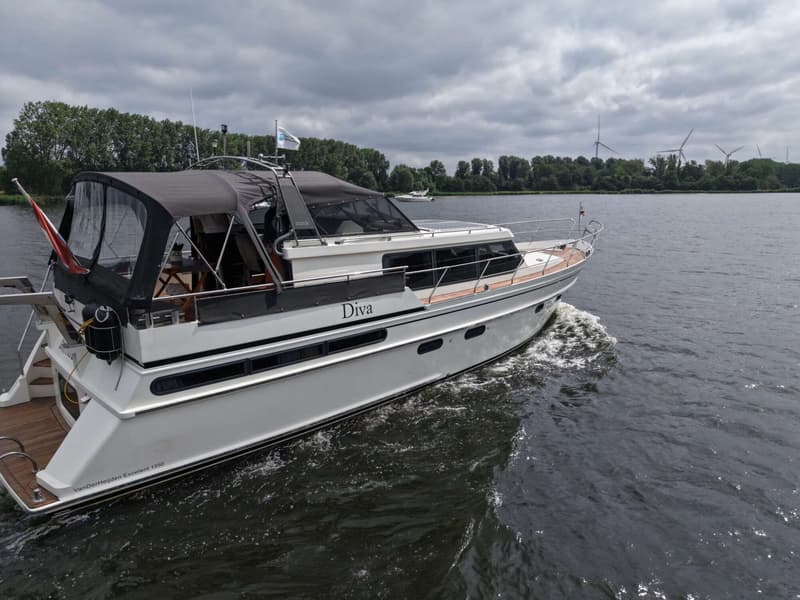 Een witte motorboot met de naam "Diva" vaart op het water, met een donkere kap en een houten dek.