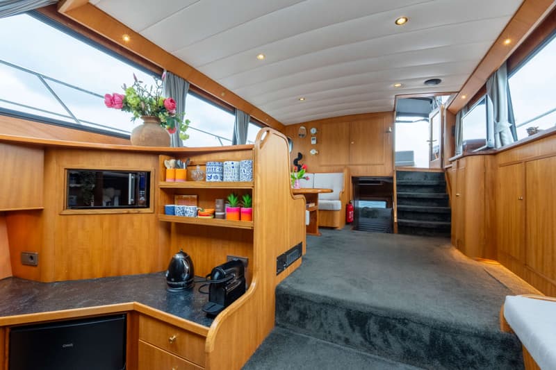 De foto toont het interieur van een boot met een keukenblok, zithoek, trap en houten afwerkingen.