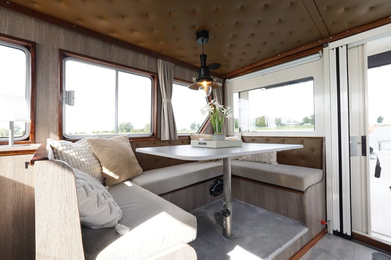 De foto toont het interieur van een boot met een zithoek, tafel, ramen en een hanglamp. — Buijs Buijs Kruiser 10.80 OK