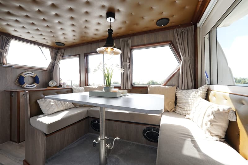 De foto toont het interieur van een boot met een zithoek, een tafel en ramen met gordijnen. — Buijs Buijs Kruiser 10.80 OK