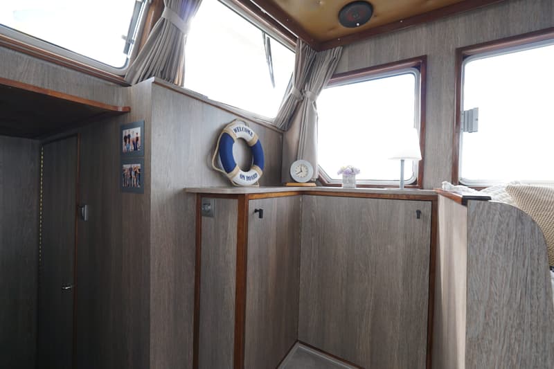 De foto toont een interieur van een boot met houten wanden, ramen met gordijnen, en decoratieve items zoals een…