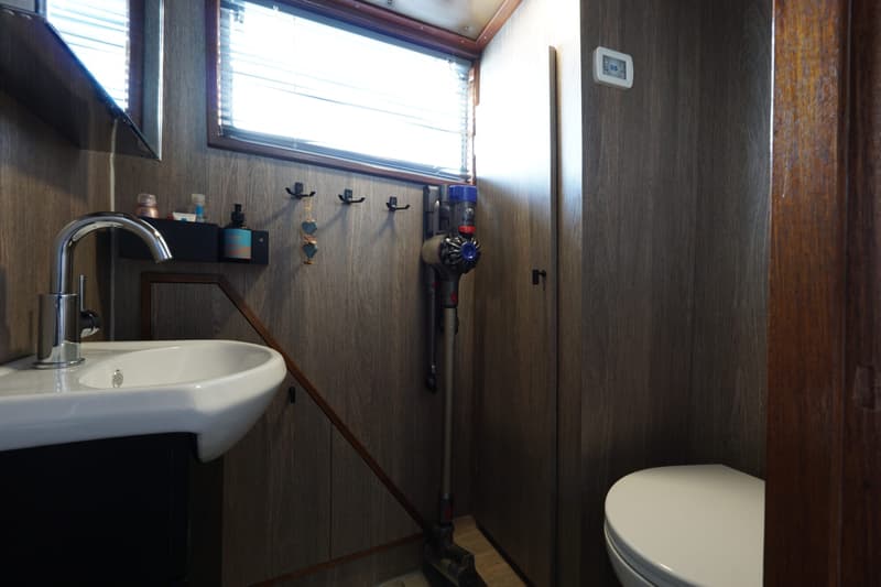 Een badkamer met een wastafel, spiegel, raam met jaloezieën, een Dyson-stofzuiger en een toilet.