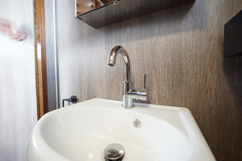 Een witte wastafel met een chromen kraan en een spiegelkastje erboven, tegen een houten wand.