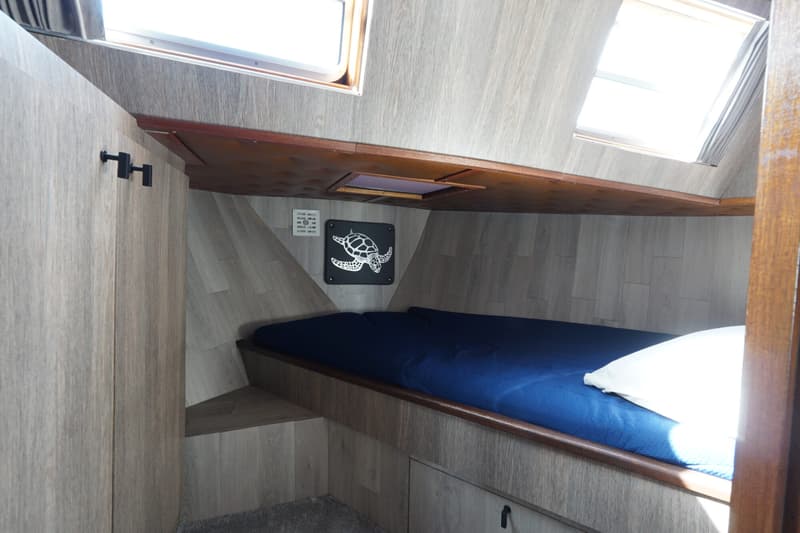 Een kajuit met een bed met blauw beddengoed, een wit kussen, en een decoratie van een schildpad aan de muur.