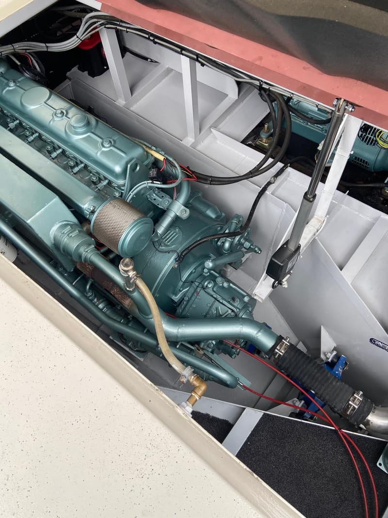 Een close-up van een lichtblauwe scheepsmotor met diverse slangen en bedrading in een motorruimte.