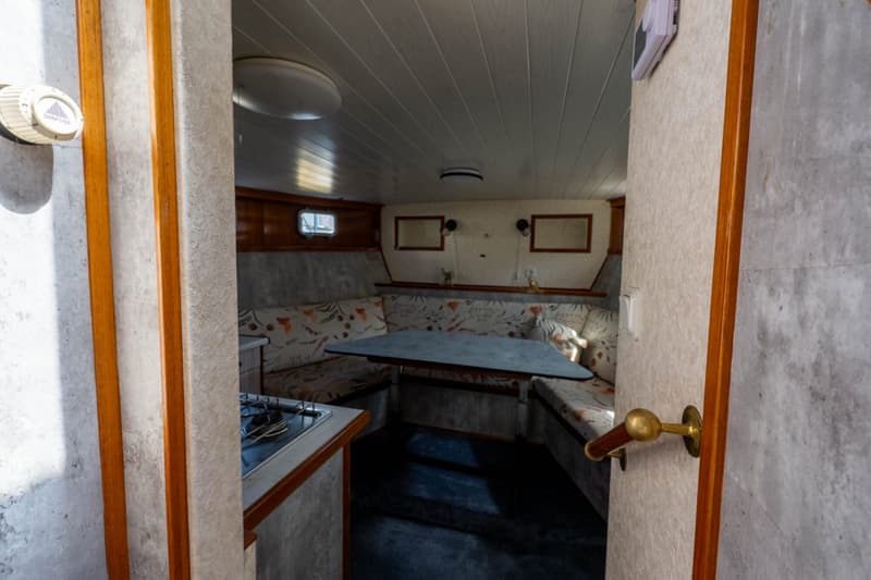 Een interieur van een boot met een zithoek, tafel en een kookplaat, gezien door een deuropening.