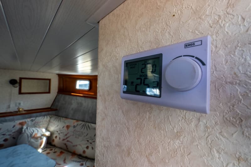 Een witte digitale thermostaat van het merk EMOS is gemonteerd op een beige wand met textuur.