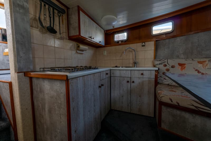 De foto toont een kombuis met een aanrecht, gootsteen, gasfornuis, keukenkastjes en een zitbank met tafel.