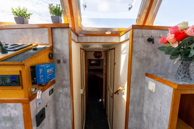 Een interieur van een boot met een doorgang naar een kajuit, een stuurstand, en een bos rozen in een vaas.