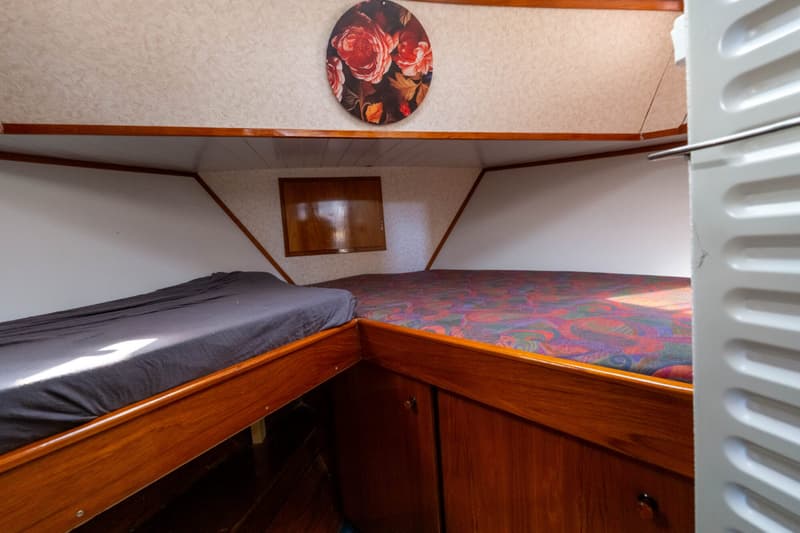 De foto toont een kajuit met twee bedden, een patrijspoort en een rond schilderij aan de wand.