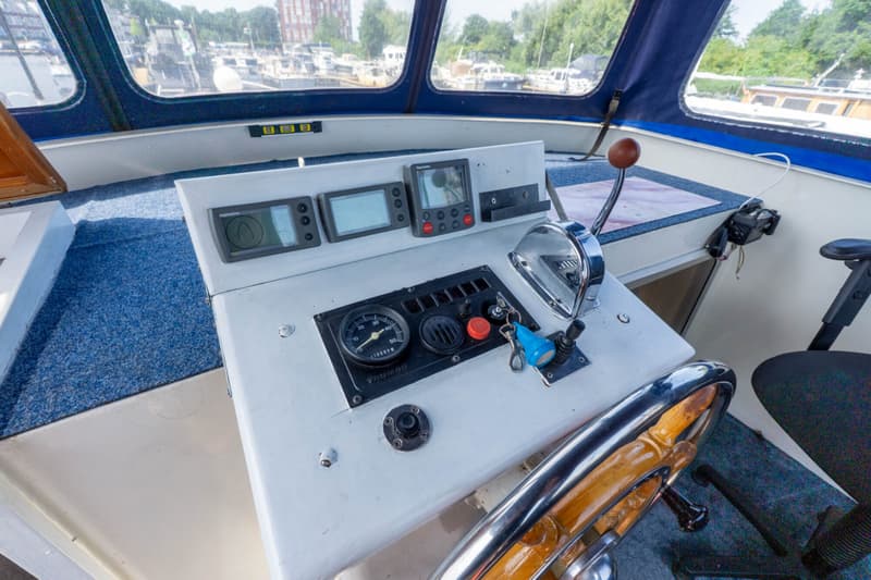 De foto toont een stuurstand met een houten stuurwiel, diverse meters en bedieningselementen, en een Raymarine display.