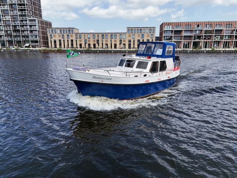 Een blauw-witte boot met de naam "Zuiderzee" vaart op het water, met gebouwen op de achtergrond.