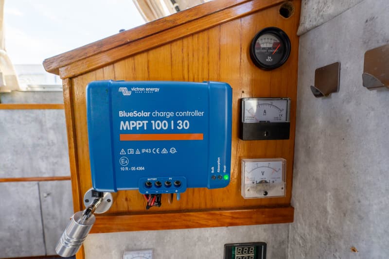 Een blauwe Victron Energy BlueSolar MPPT 100 | 30 laadregelaar is gemonteerd op een houten paneel, met diverse meters…