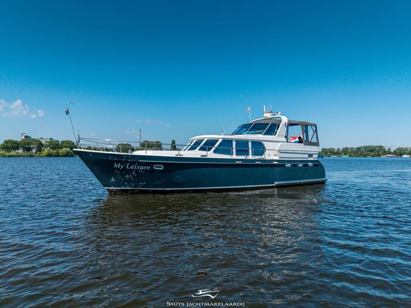 Een blauw-witte motorboot met de naam "My Leisure" vaart op een zonnige dag over rustig water.