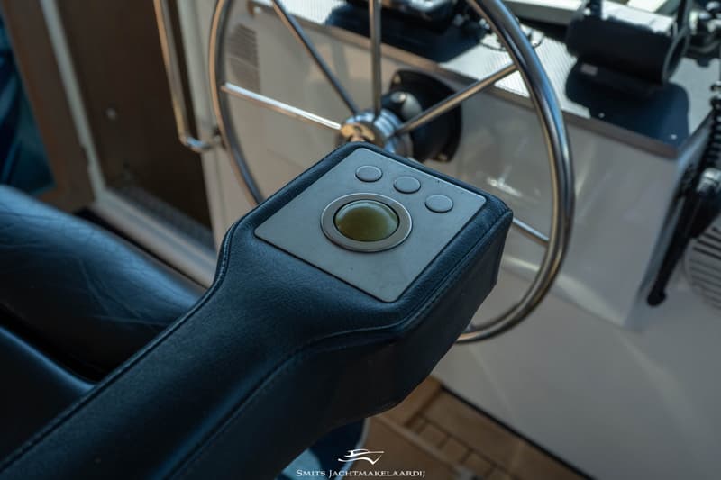 Een close-up van een zwarte, lederen armleuning met een ingebouwd bedieningspaneel met een trackball en drie knoppen.