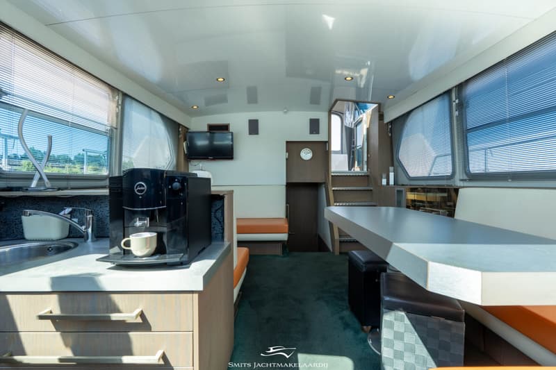Een interieur van een boot met een keukenblok, een eettafel met banken, een trap en een televisie.