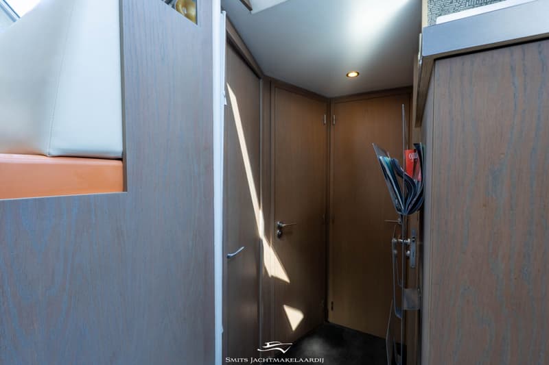 Een interieur van een boot met houten wanden, een witte en oranje bank, en een rek met tijdschriften.