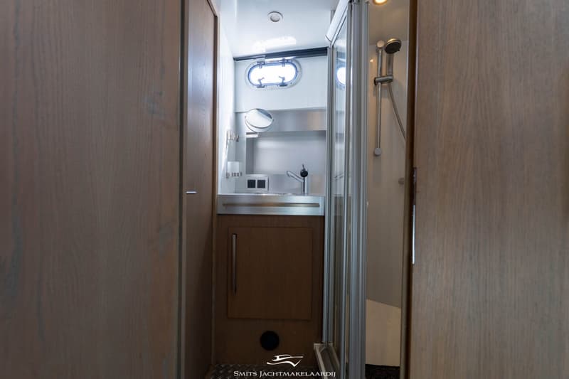 Een badkamer met een wastafel, spiegel, patrijspoort, douchecabine en een douchekop.