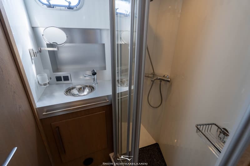 Een badkamer met een wastafel, spiegel, douche en een patrijspoort is te zien.