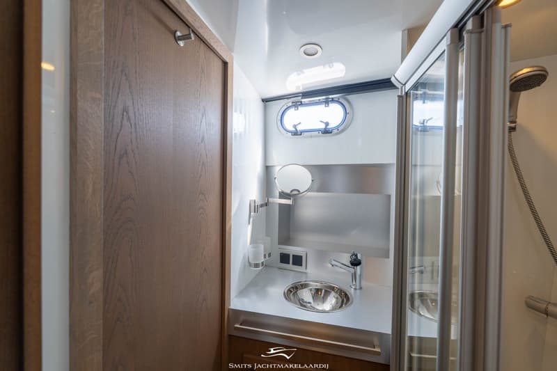 Een badkamer met een houten deur, een patrijspoort, een wastafel met spiegel en een douchecabine.