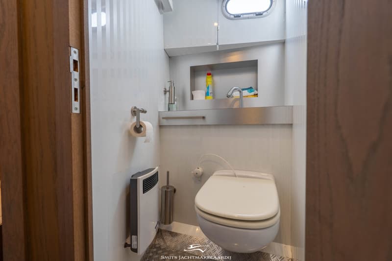 Een witte toiletruimte met een toilet, wastafel en een klein raam, gezien vanuit een deuropening.