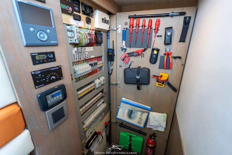 Een open kast met een elektrisch paneel, diverse gereedschappen, handleidingen en een brandblusser.