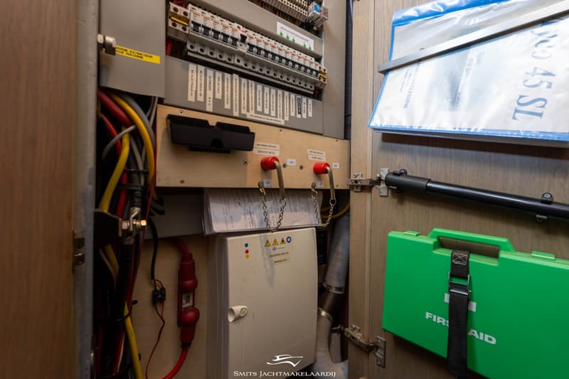 Een open kast met een elektrisch paneel, bedrading, een groene EHBO-doos en documenten.