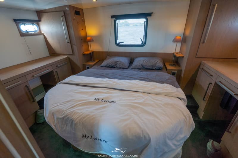 Een slaapkamer in een boot met een tweepersoonsbed, twee nachtkastjes met lampen, en kasten aan weerszijden.