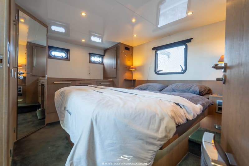 Een slaapkamer met een tweepersoonsbed, twee patrijspoorten, een raam en een spiegel.