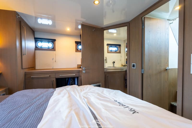 Een kajuit met een bed, houten kasten, patrijspoorten en een open deur naar een badkamer met wastafel.