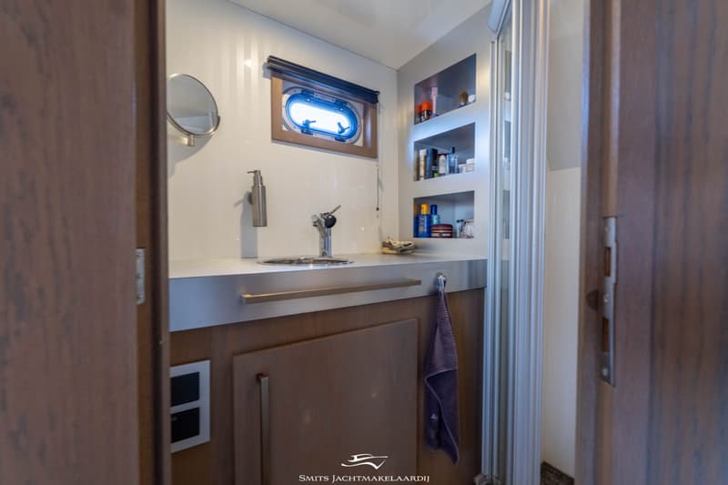 Een badkamer met een wastafel, spiegel, patrijspoort, opbergplanken met toiletartikelen en een douchecabine.