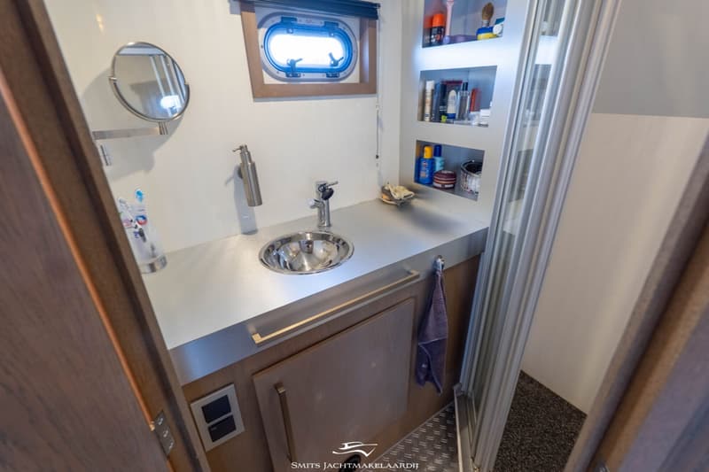 Een badkamer in een boot met een wastafel, spiegel, patrijspoort, opbergplanken en een douchecabine.