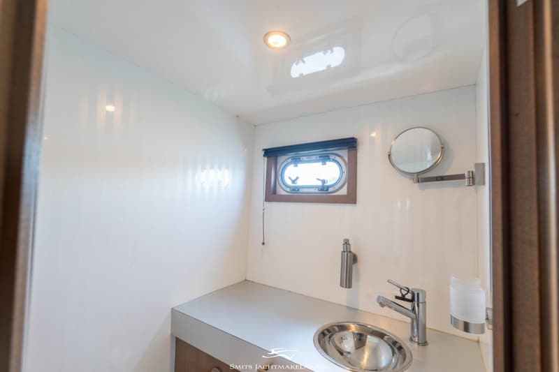 Een witte badkamer met een patrijspoort, een wastafel met kraan en een uitschuifbare spiegel.