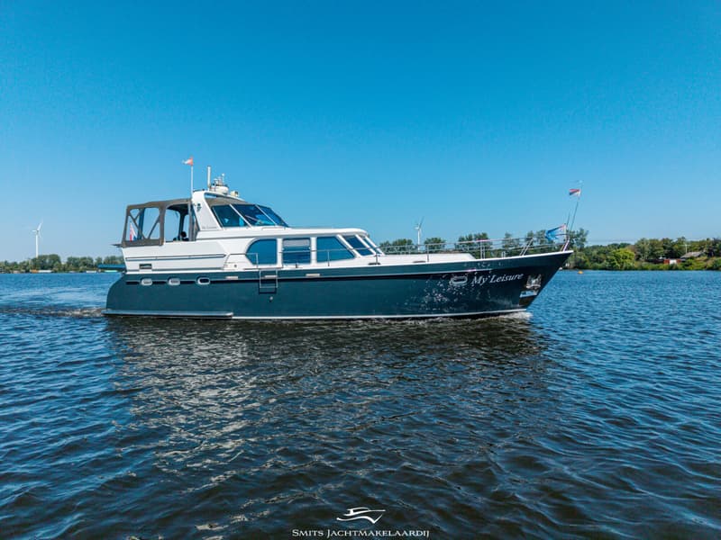 Een blauw-witte motorboot met de naam "My Leisure" vaart op een waterweg onder een helderblauwe lucht.
