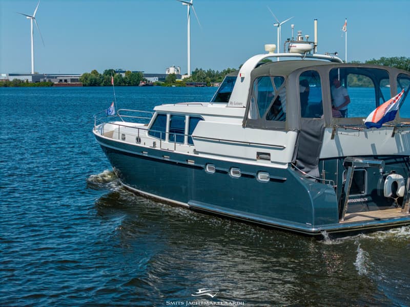 Een blauw-witte motorboot vaart op het water, met een man aan het roer en windmolens op de achtergrond.