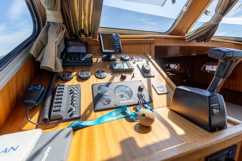 De foto toont een houten dashboard met diverse navigatie-instrumenten, een Yanmar-paneel en een TFX-gashendel.