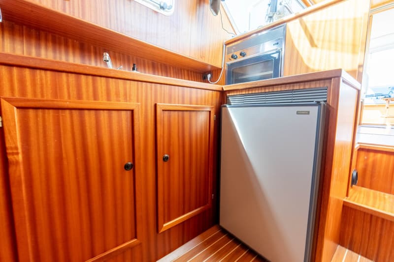 Een houten interieur met een ingebouwde oven, een koelkast en twee kastjes.