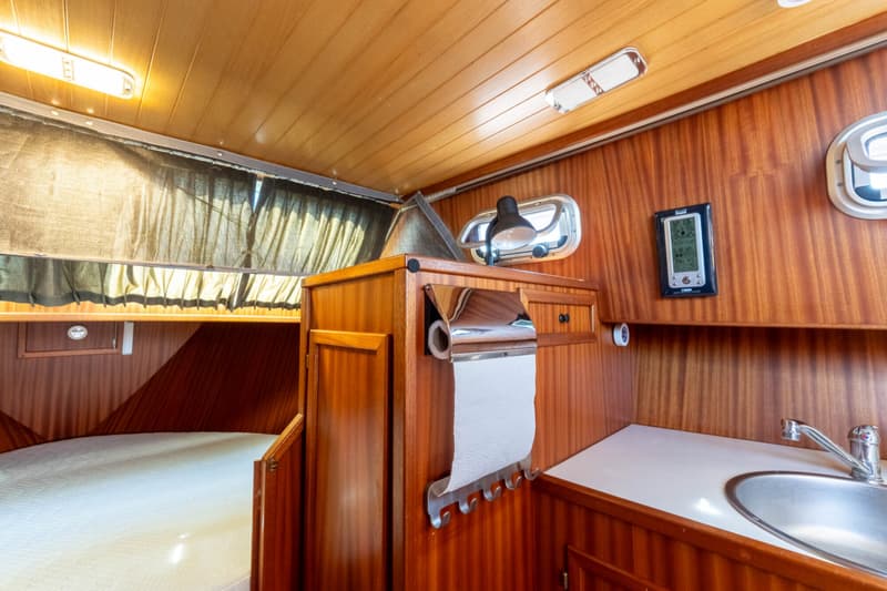 De foto toont een kajuit met een bed, een aanrecht met spoelbak, een papieren handdoekhouder en houten wanden en plafond.