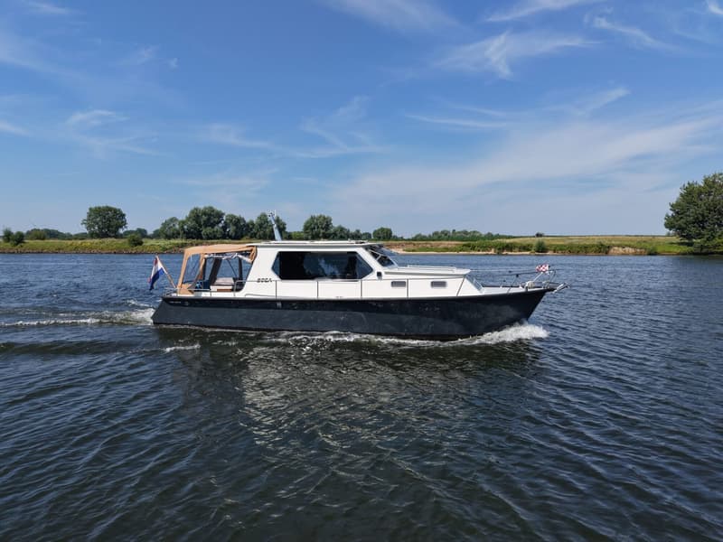 Een witte en donkerblauwe motorboot met een oranje kap vaart op een rivier onder een blauwe lucht.