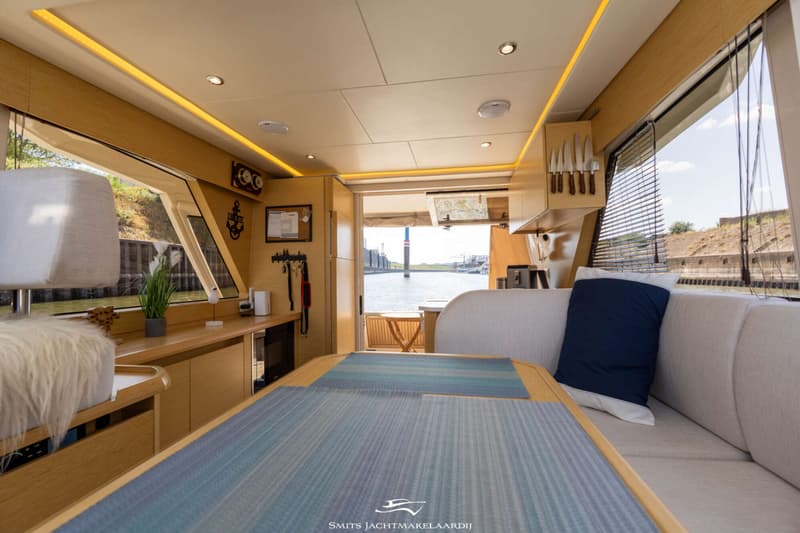 Een interieur van een boot met een houten tafel, banken, een keukenblok en uitzicht op water. — Greenline Greenline 39